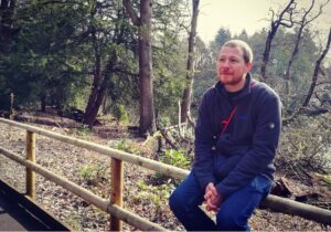 Me sat on a wooden fence with a forest in the background